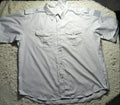 A light gray short-sleeve button-up shirt with two chest pockets, laid flat on a white shaggy blanket.