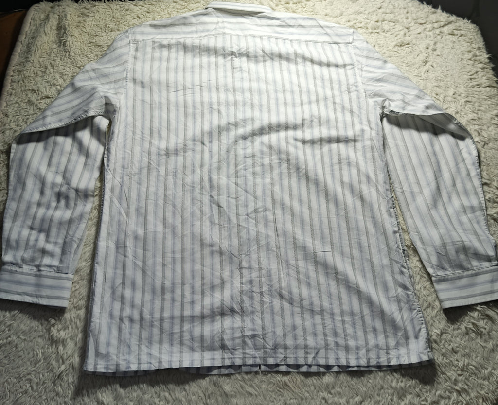 A long-sleeve button-up shirt with vertical light blue and white stripes, laid flat on a textured white shag rug. The photo is taken from above and includes a camera settings overlay at the bottom.