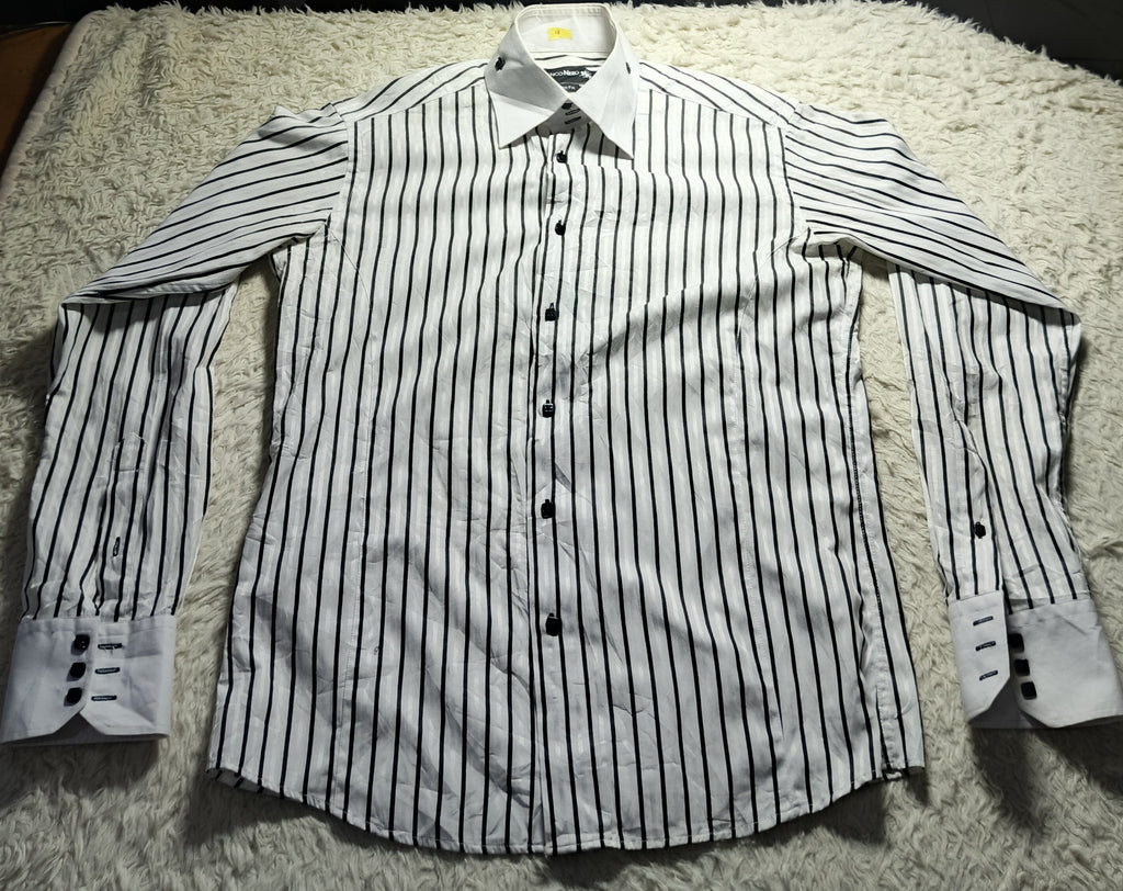 A long-sleeve button-up dress shirt with thin black vertical pinstripes on a white base, laid flat on a white shag rug. A small LED light is shining onto the shirt from above, with chairs and a red garment visible in the background.
