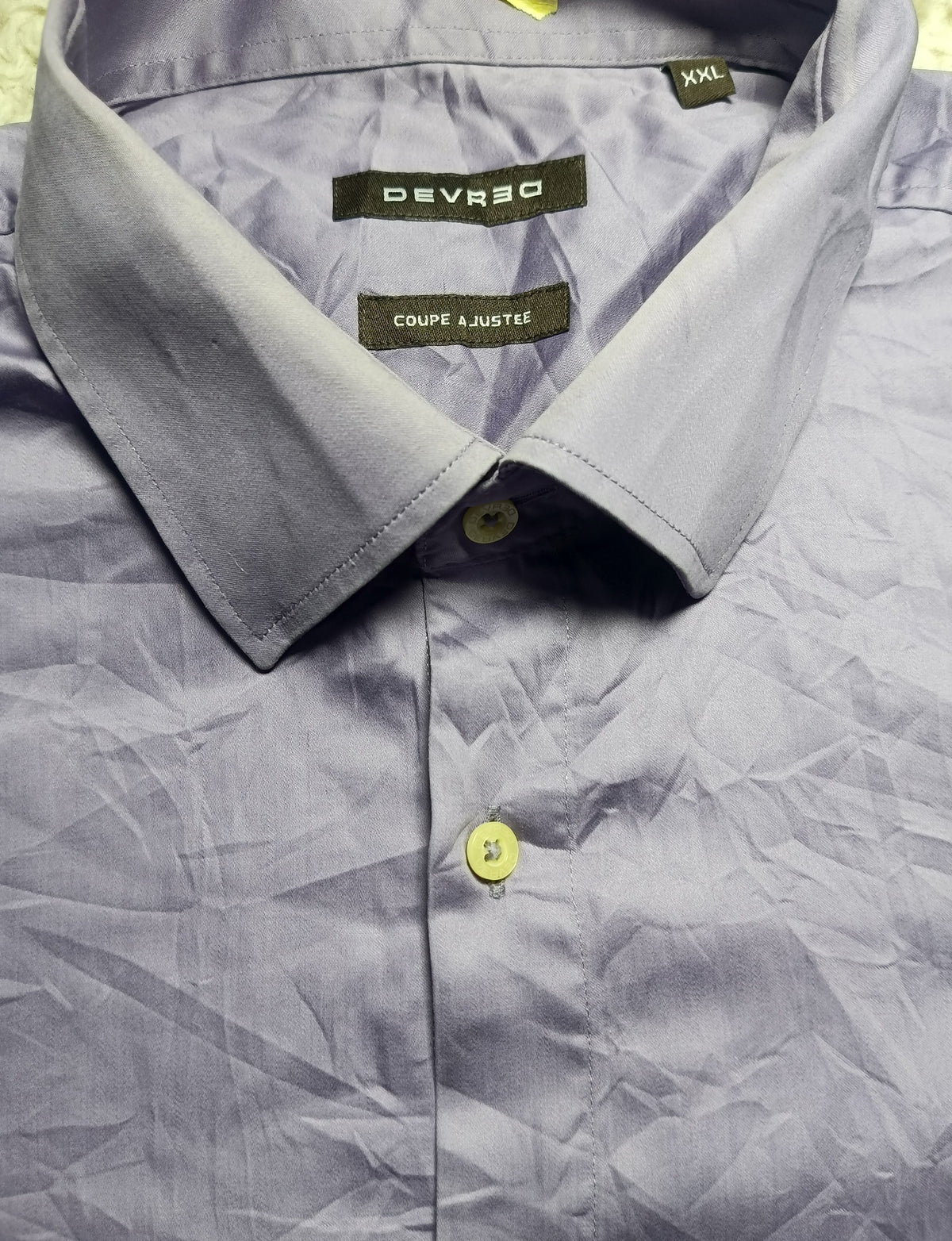 A close-up of a light blue-gray collared shirt by Deverso, showing the inner neck label, collar, and front button. The shirt has a crinkled texture and is photographed flat against a neutral background.