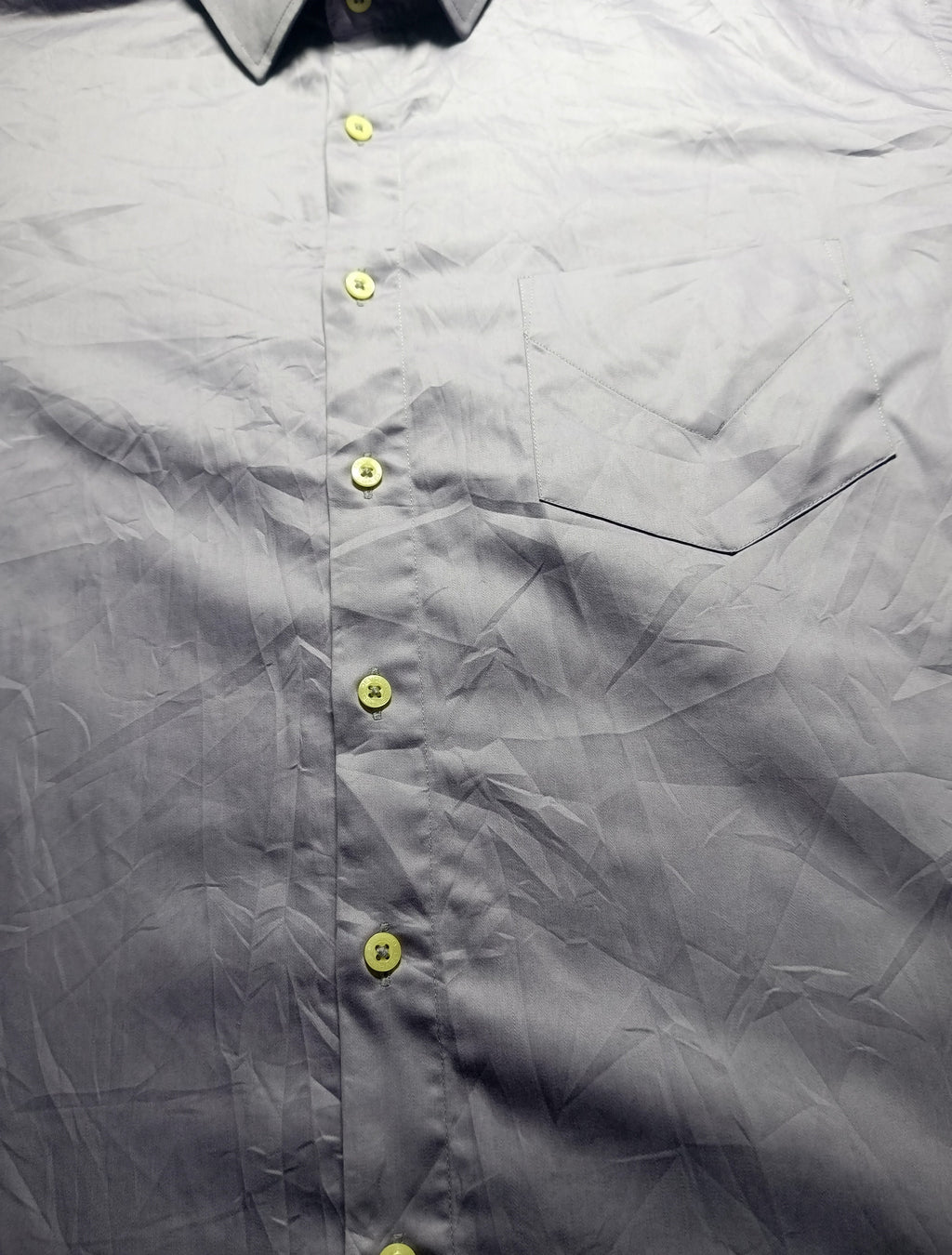 Close-up of a gray button-down shirt with yellow buttons, showing the collar, front placket, chest pocket seam, and wrinkled fabric texture.