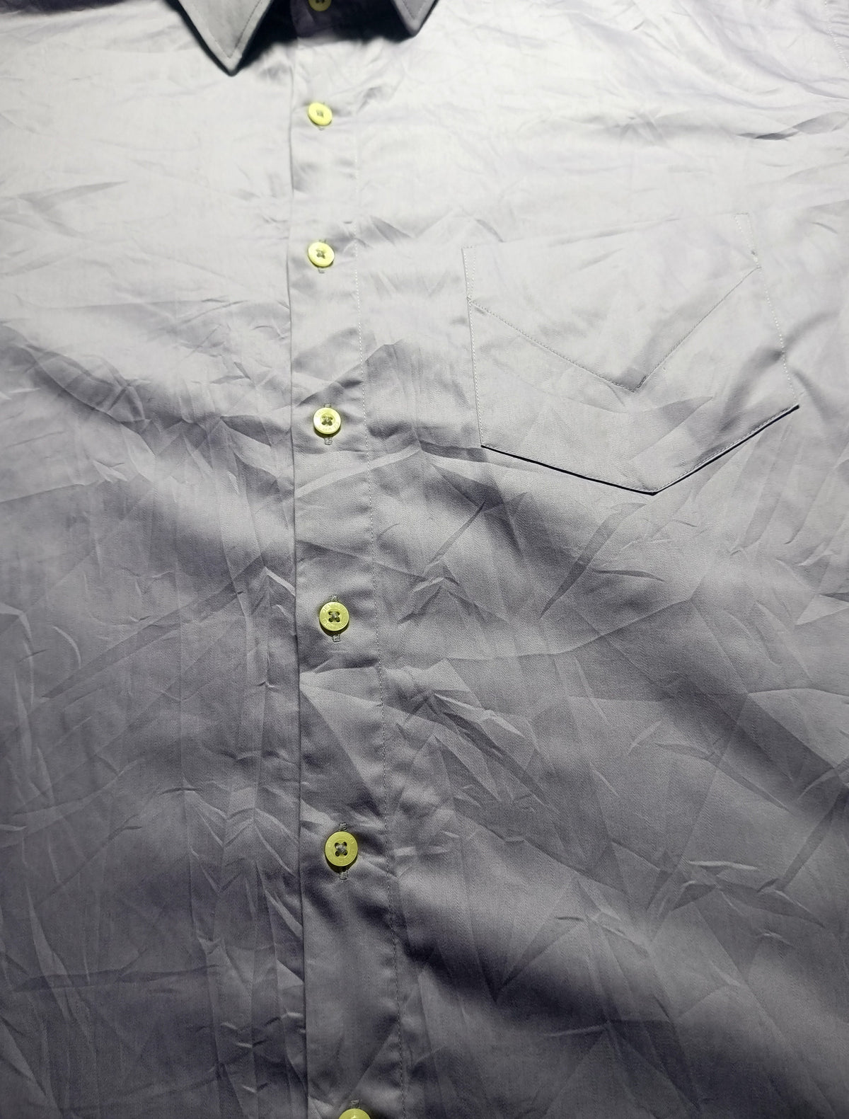 Close-up of a gray button-down shirt with yellow buttons, showing the collar, front placket, chest pocket seam, and wrinkled fabric texture.