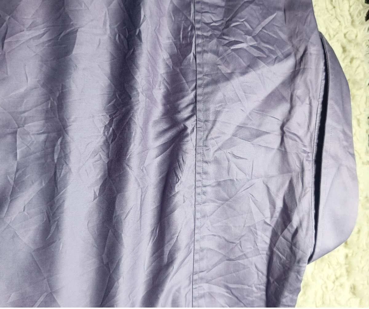 A close-up of a wrinkled lavender-purple fabric surface, likely part of a garment, with a white textured rug visible on the right side. A camera settings watermark is visible at the bottom.