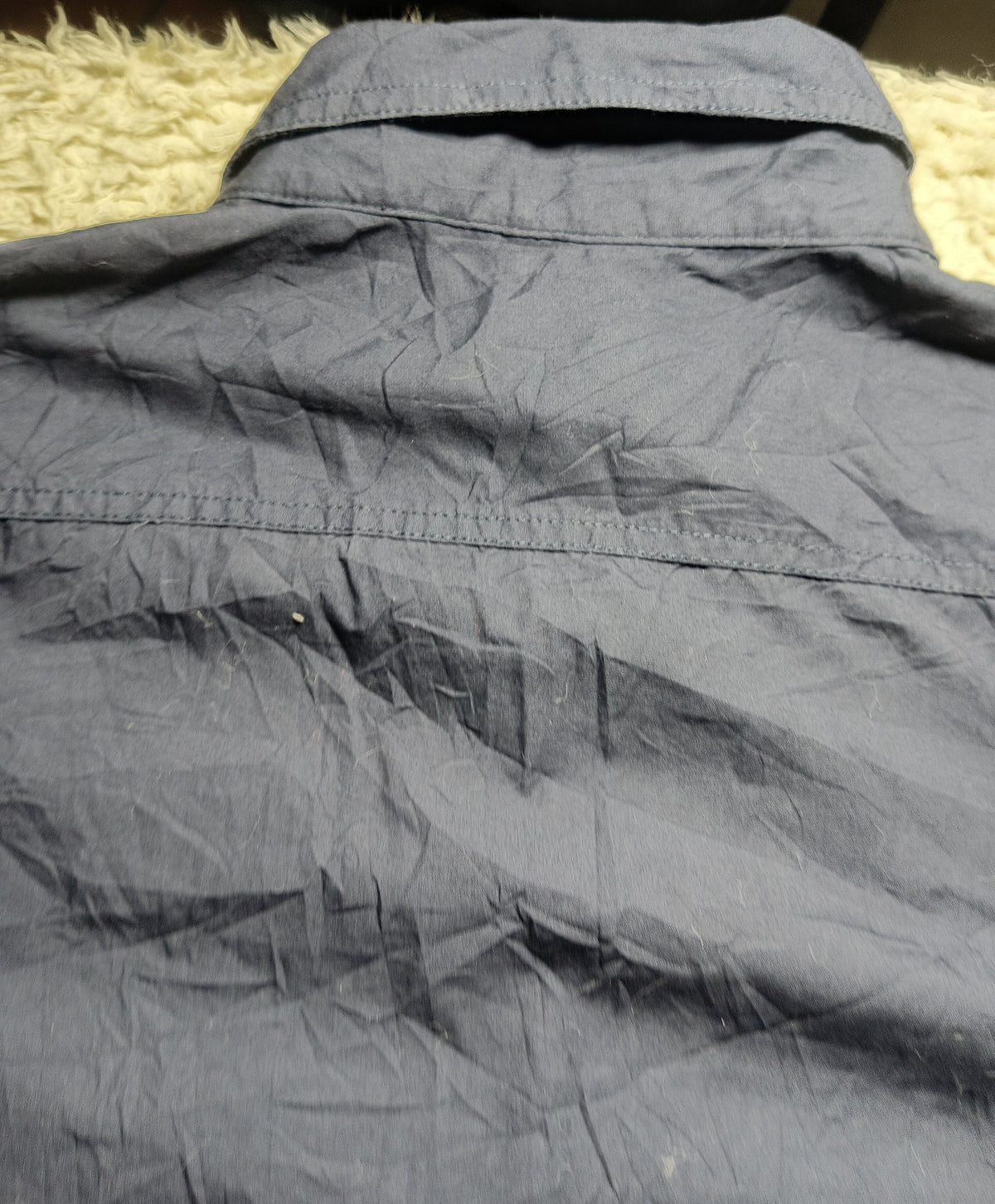 A close-up of a dark gray crinkled fabric, likely a shirt or jacket, laid flat on a textured cream surface. The image has a camera watermark at the bottom reading 'POVA 6 Neo 23mm f/1.