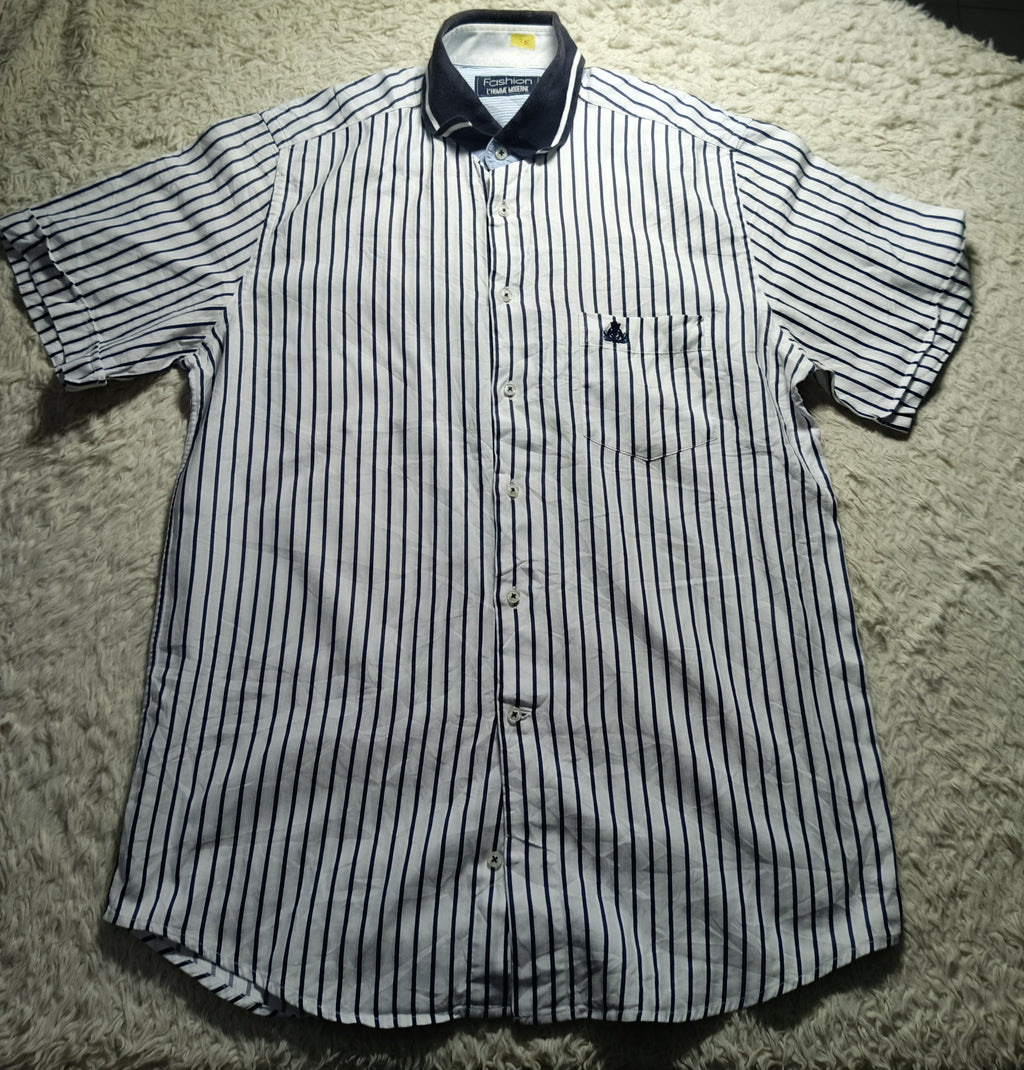 A short-sleeve button-up shirt with thin vertical navy blue stripes on a white background, laid flat on a white shag rug. The shirt features a dark navy collar and a small embroidered logo on the left chest pocket.
