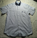 A short-sleeve button-up shirt with thin vertical navy blue stripes on a white background, laid flat on a white shag rug. The shirt features a dark navy collar and a small embroidered logo on the left chest pocket.