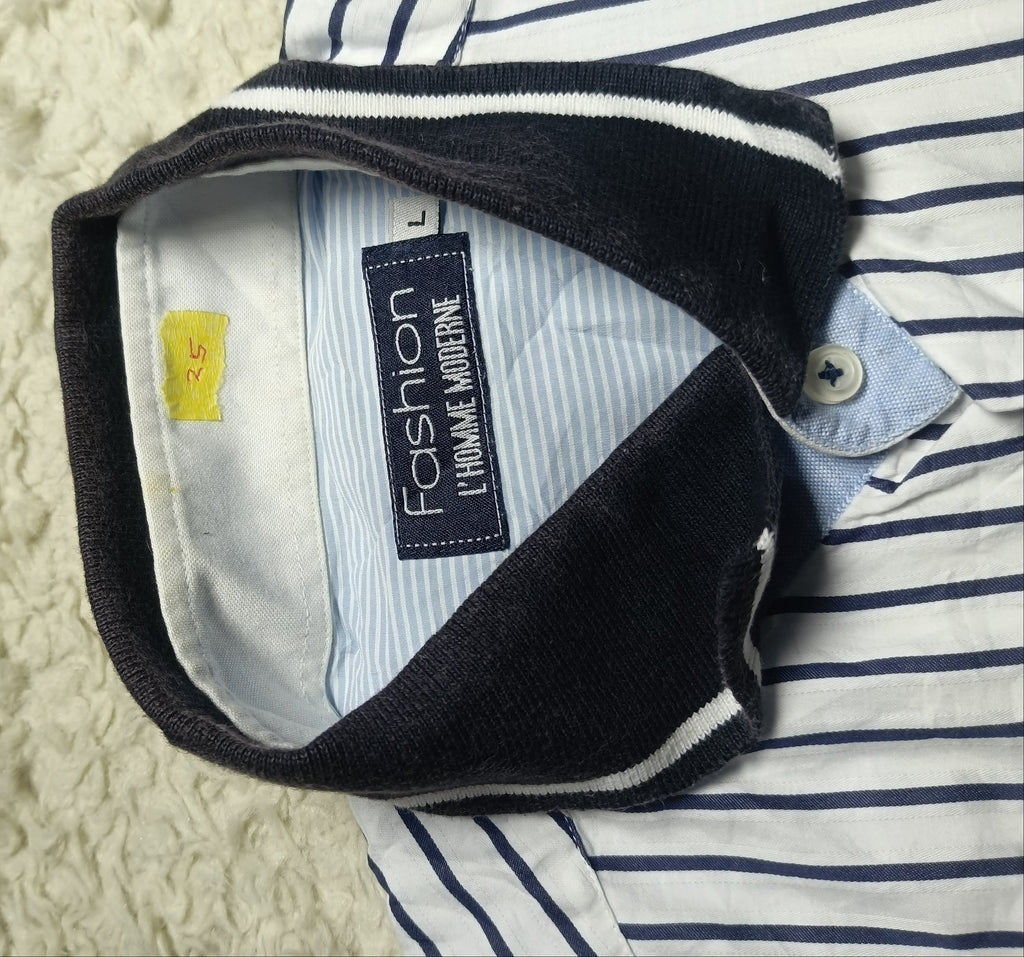 Close-up of a striped button-up shirt laid flat on a white textured blanket, with the collar turned up to show the inside neck label reading 'Fashion 1 Volume Worldwide'.