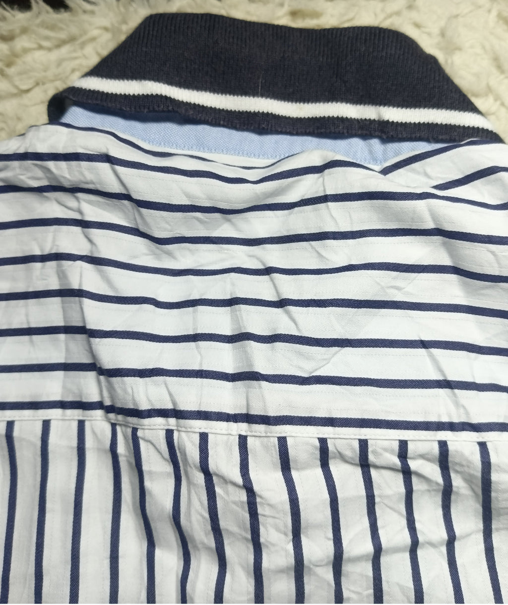 A folded white knit garment with navy blue horizontal stripes across the upper section and vertical navy stripes on the lower section, laid on a white shaggy surface.