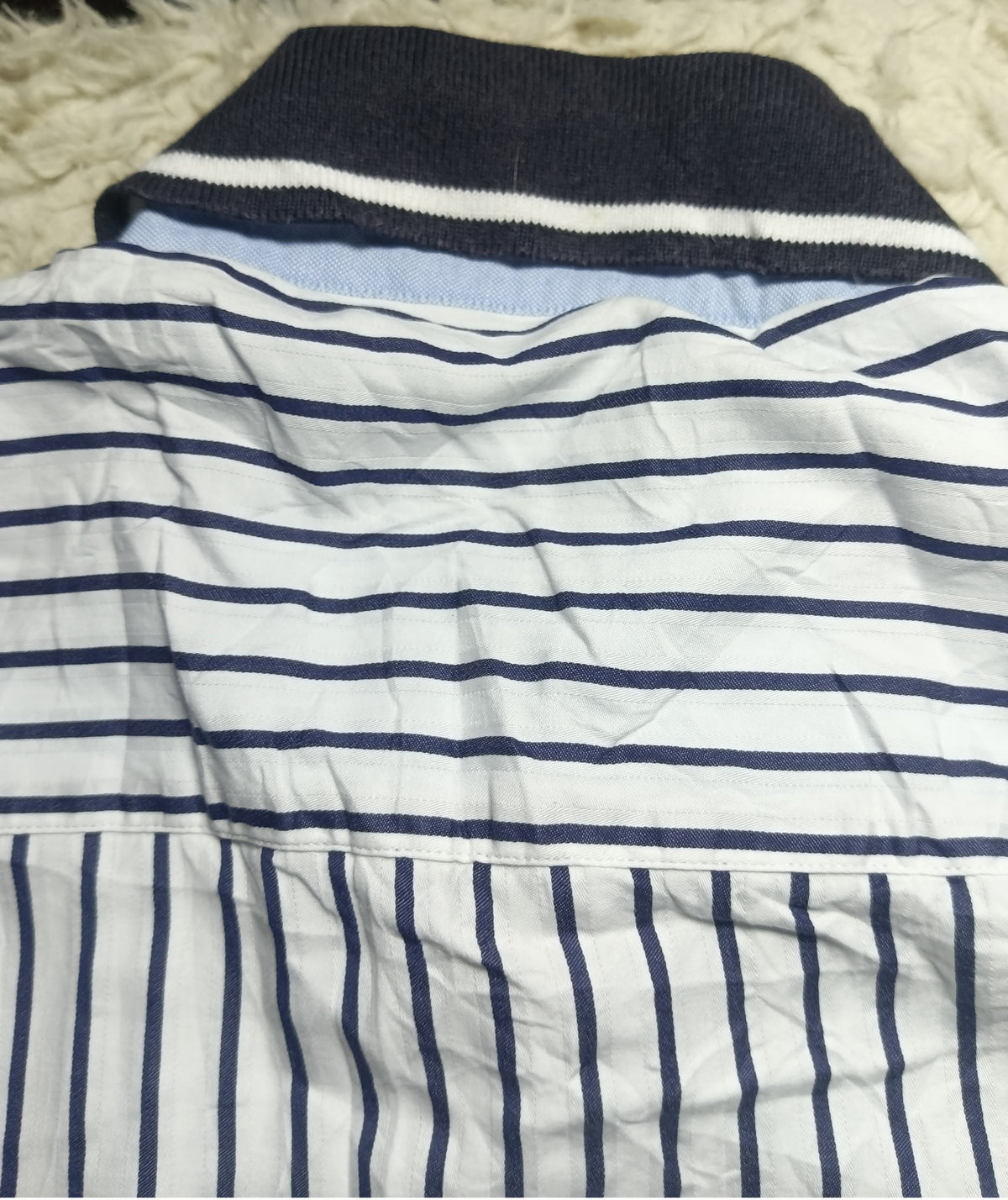A folded white knit garment with navy blue horizontal stripes across the upper section and vertical navy stripes on the lower section, laid on a white shaggy surface.
