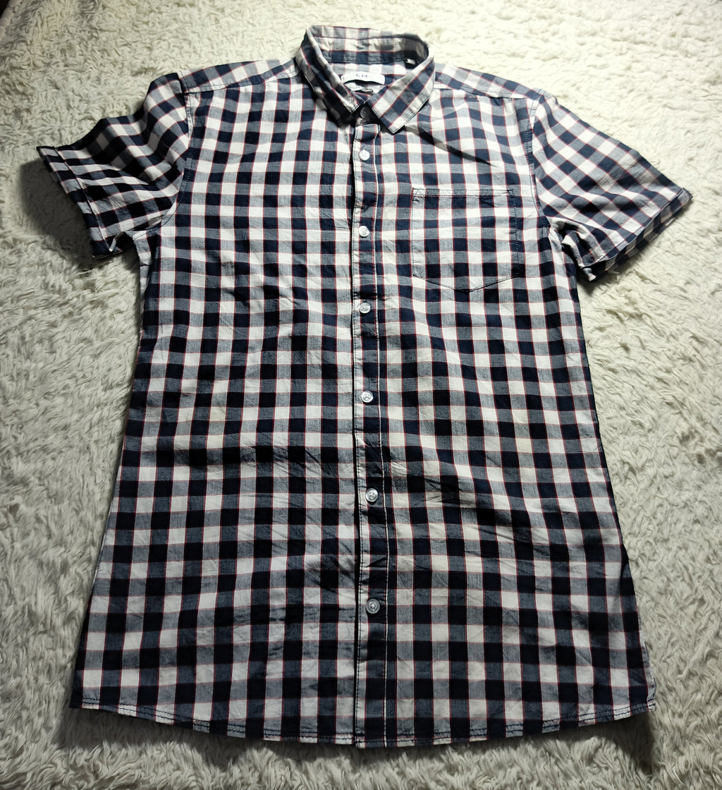 A short-sleeve button-up shirt with a black and white checkered pattern, laid flat on a white shag rug.