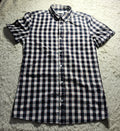 A short-sleeve button-up shirt with a black and white checkered pattern, laid flat on a white shag rug.