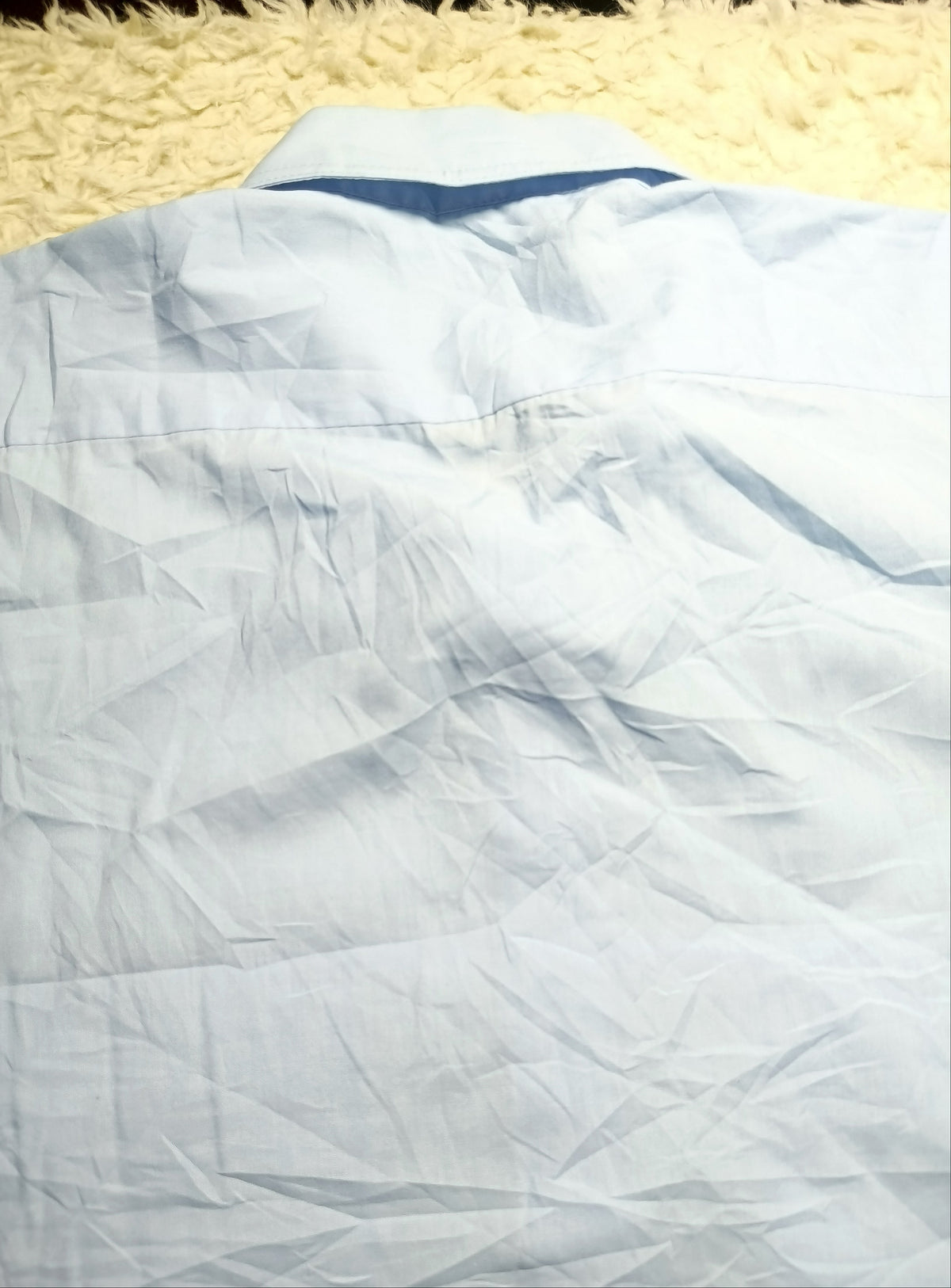 A close-up of a light blue wrinkled fabric, likely a shirt or garment, laid on a textured cream rug. A white camera-info strip is at the bottom with the text 'POVA 6 Neo' and '23mm f/1.