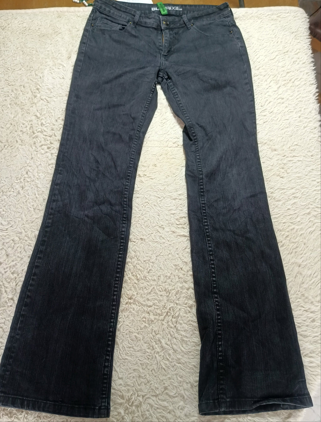 A pair of dark gray flare jeans laid flat on a white textured blanket, with a wooden table and store fixtures visible in the background.