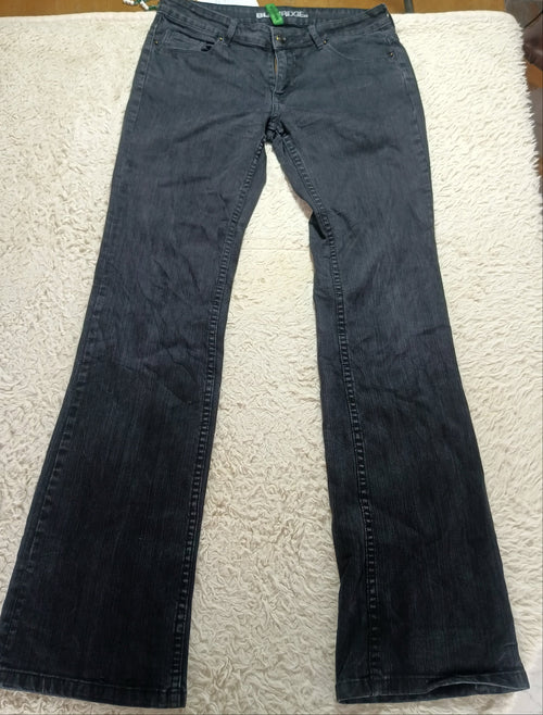 A pair of dark gray flare jeans laid flat on a white textured blanket, with a wooden table and store fixtures visible in the background.