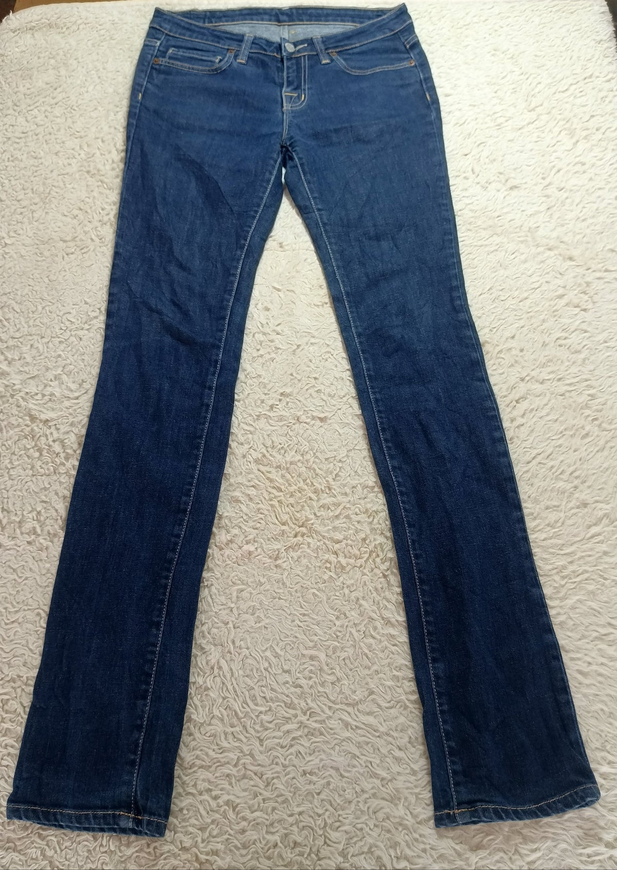 A pair of medium-wash blue denim jeans laid flat on a white textured blanket, photographed from above.