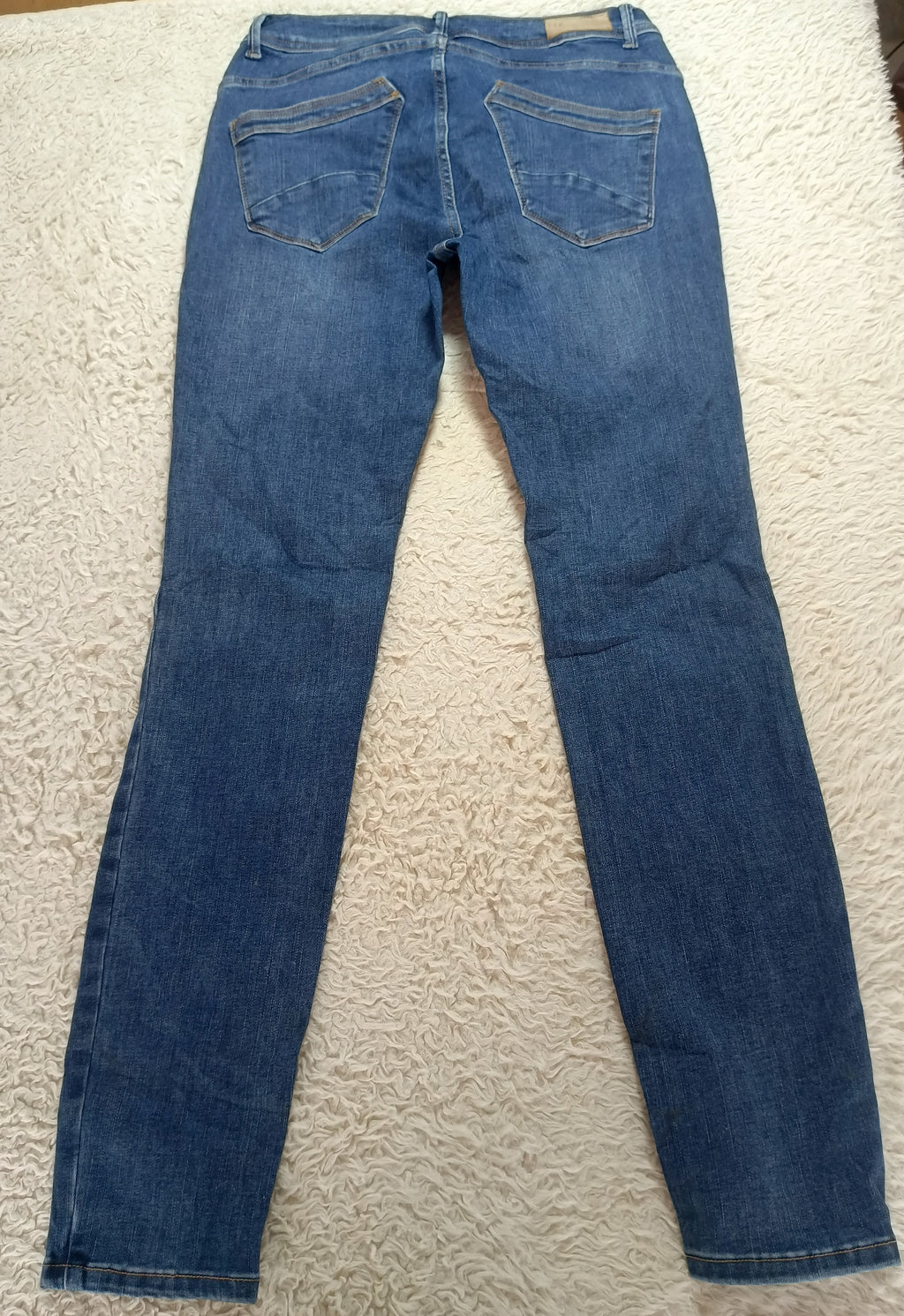 A pair of blue denim jeans laid flat on a white textured rug, showing the back pockets and waistband.