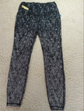 Black and white patterned leggings laid flat on a textured beige carpet. The leggings feature an abstract, leaf-like pattern in black and white, with a small yellow tag near the waistband.