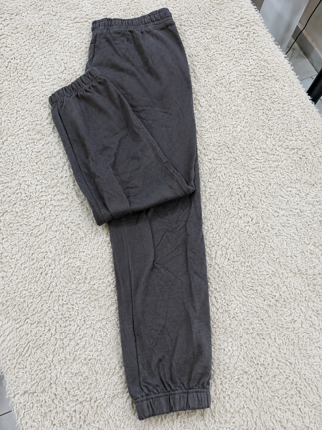 Dark gray jogger pants with elastic waistband and ankle cuffs, laid flat on a beige textured rug.