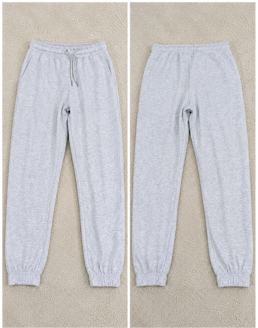 Light heather gray jogger sweatpants shown from both front and back views on a beige textured background, with size and style codes printed below each pair.