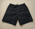 Black lightweight drawstring shorts laid flat on a beige carpet background, with a small visible Patagonia logo near the lower right leg.