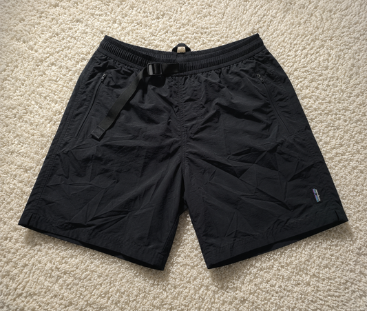 Black lightweight drawstring shorts laid flat on a beige carpet background, with a small visible Patagonia logo near the lower right leg.