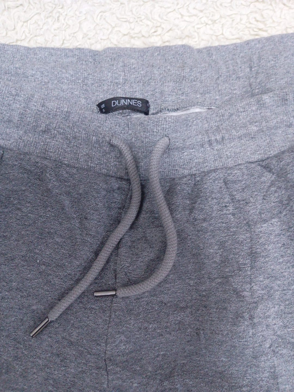 Close-up of a pair of heather gray sweatpants showing the waistband, drawstring, and a black DUNNIES brand label.