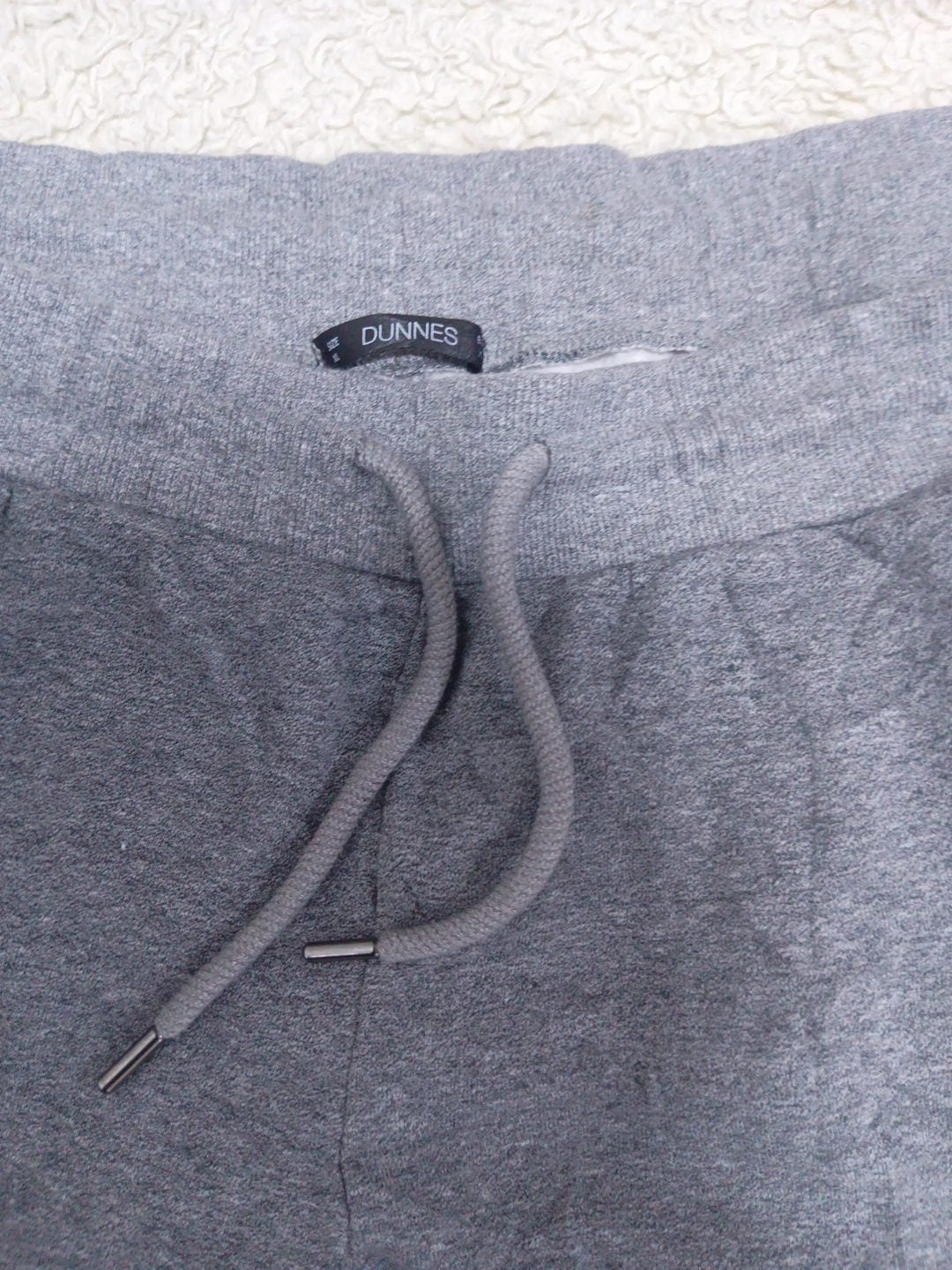 Close-up of a pair of heather gray sweatpants showing the waistband, drawstring, and a black DUNNIES brand label.